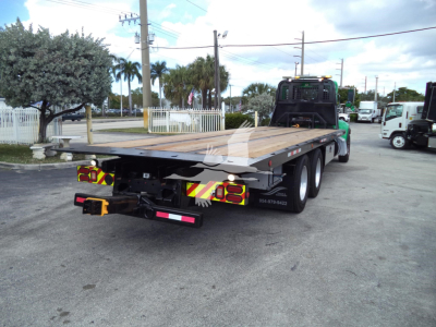 Rear view of a black flatbed rollback tow truck with wooden deck and yellow/red reflective chevrons.