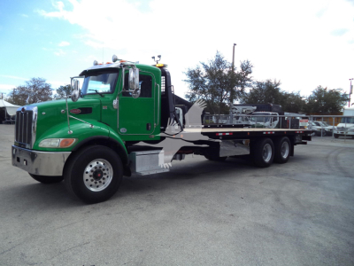 Green Peterbilt rollback tow truck with long flatbed, cab front showing Peterbilt emblem and dual mirrors.