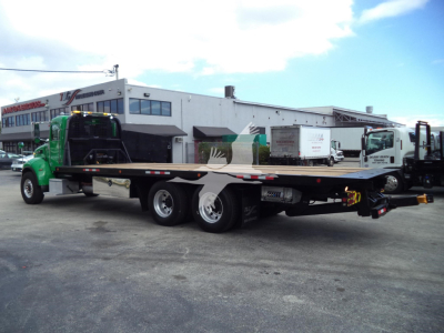Peterbilt 348 rollback truck in a parking lot, green cab, long flatbed, various equipment