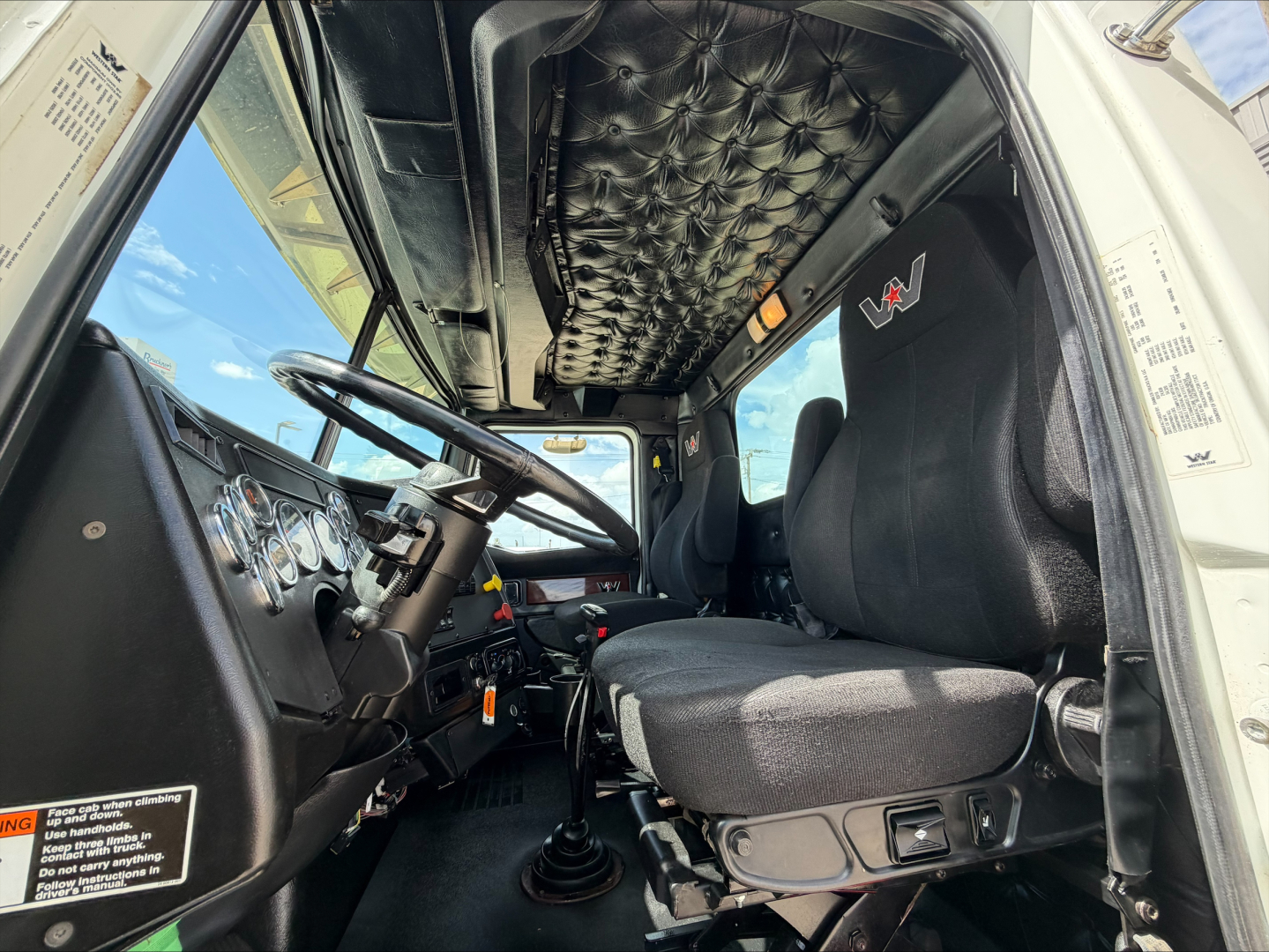 Truck cab interior showing steering wheel, dashboard, and seat with quilted overhead lining; driver side view inside a 2019 Western Star 4900 SF.