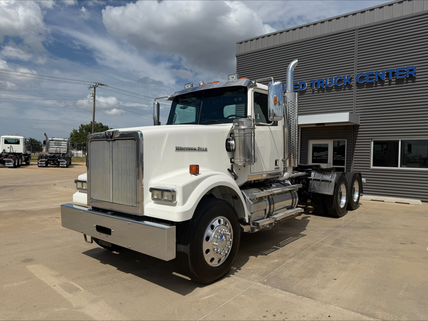 2019 Western Star 4900 SF tractor-trailer in front of dealership showing chrome grille, white cab, dual rear axles, side steps, and fuel tanks.