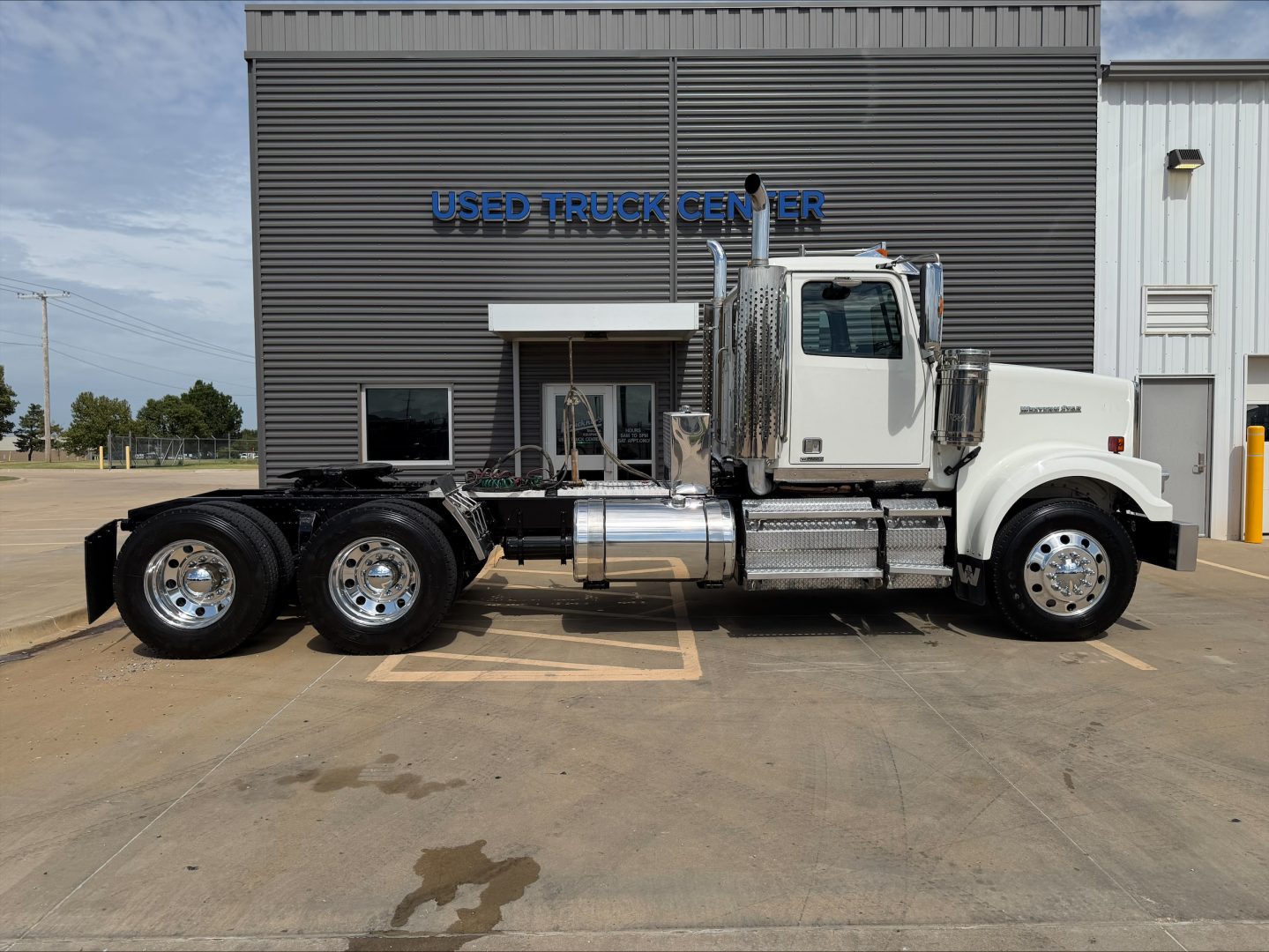 2019 Western Star 4900 SF conventional daycab truck side view showing chassis, fuel tanks, exhaust stack, and dual rear axles in front of a Used Truck Center building.