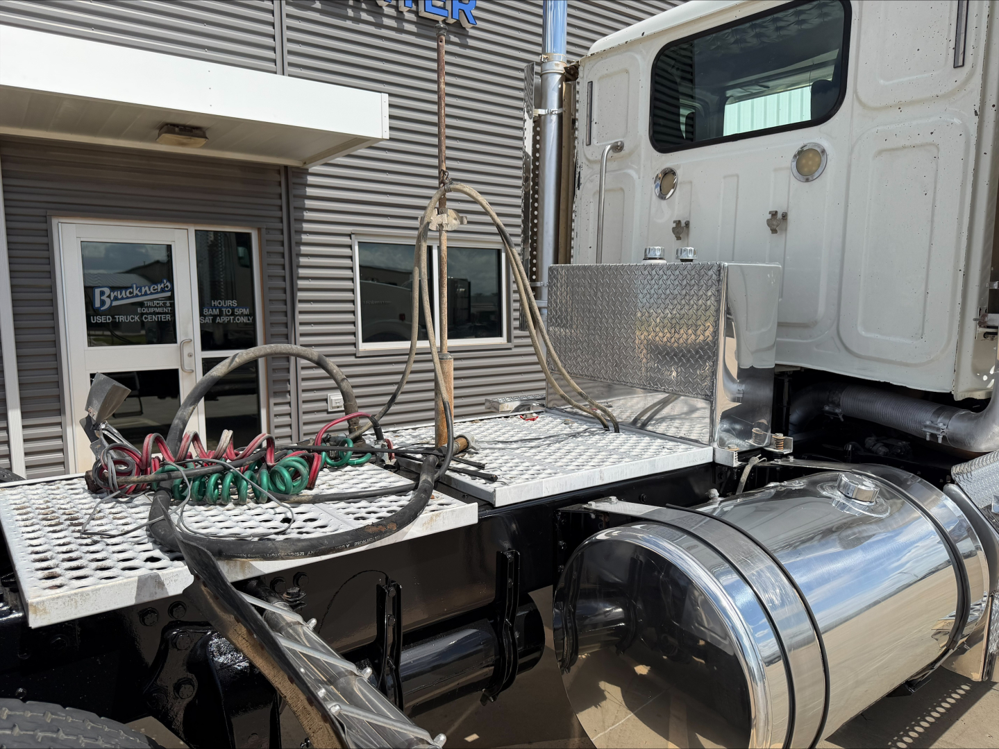 Truck cab area showing chrome cylindrical fuel tanks and diamond plate platform with hoses and wiring on a Western Star 4900 SF convention daycab, side view.