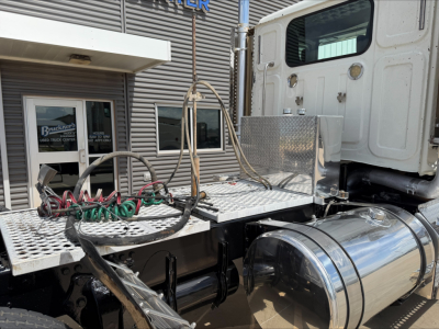 Truck cab area showing chrome cylindrical fuel tanks and diamond plate platform with hoses and wiring on a Western Star 4900 SF convention daycab, side view.