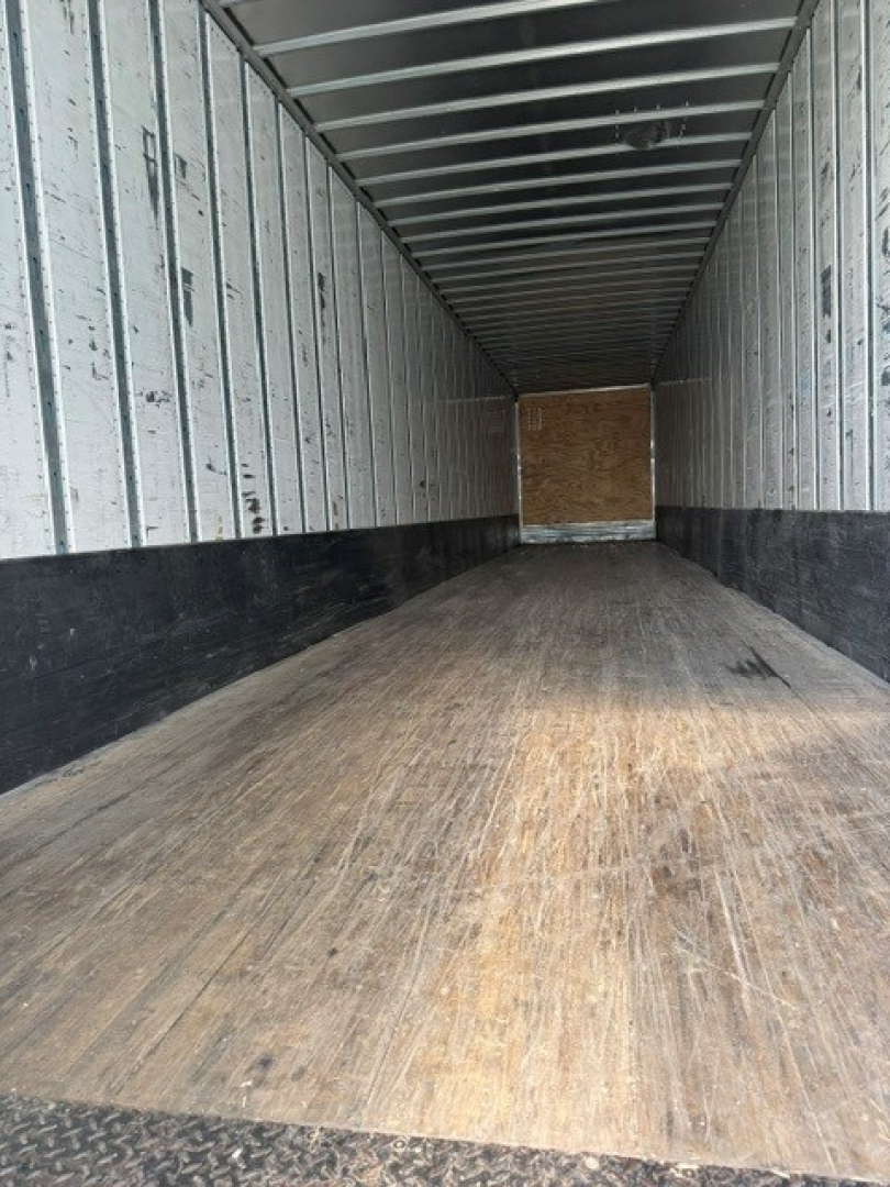 Utility trailer interior showing wooden floor and metal side walls with ribbed ceiling, empty cargo area.