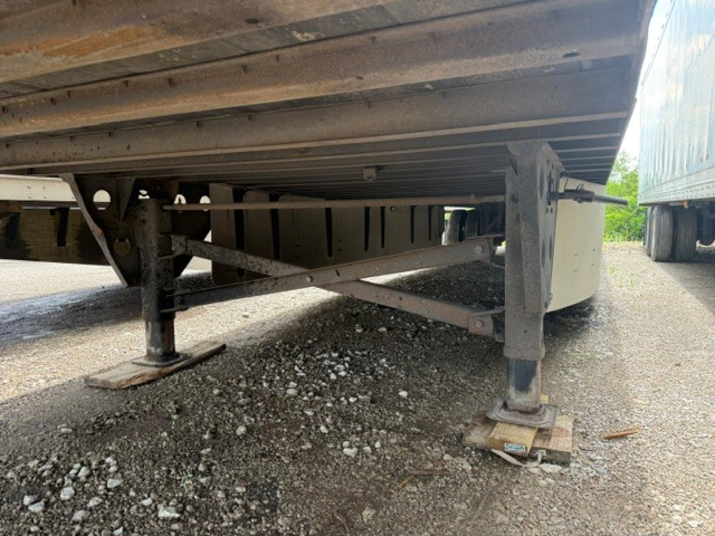 Underbelly of a utility trailer showing support legs, frame rails, and ground contact pads.
