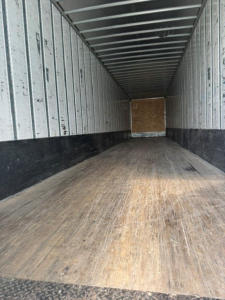 Utility trailer interior showing wooden floor and metal side walls with ribbed ceiling, empty cargo area.