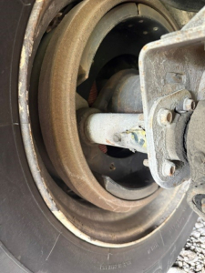 Wheel hub and suspension components of a utility trailer, showing a circular rim, axle spindle, and mounting hardware.