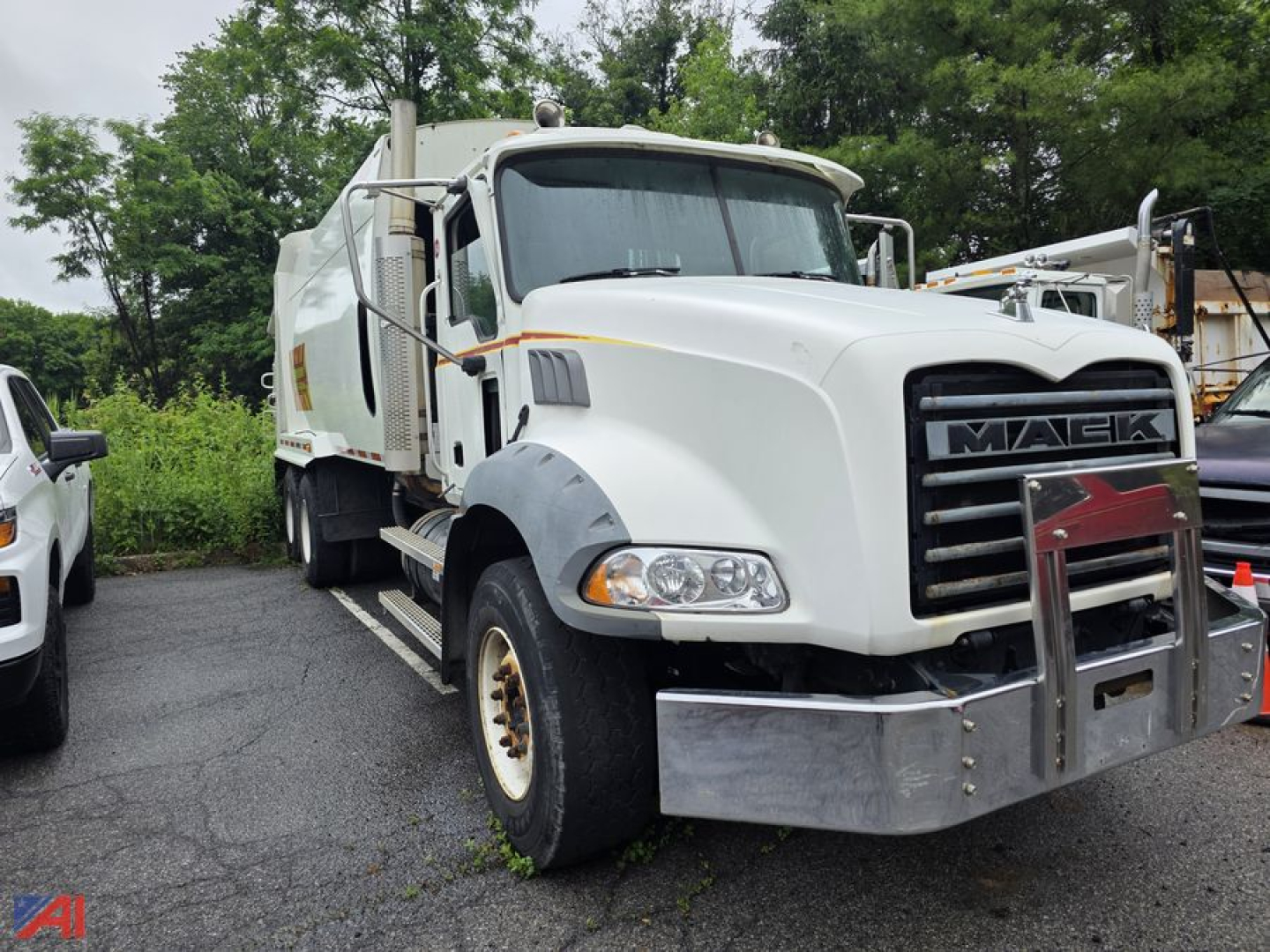 Mack Granite garbage truck front-left view in-service showing large chrome bumper and grille, white cab with black hood vents, and side mirrors.