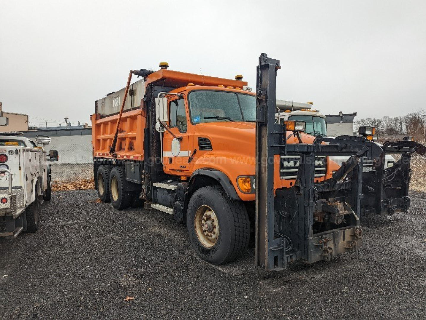 Orange 2004 Mack CV713 Granite plow truck side view showing front plow and salt spreader, VIN visible from photo, stock number in listing.