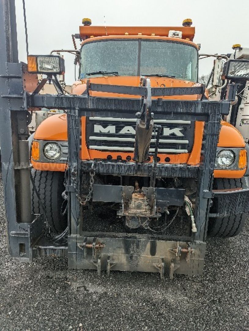 Front view of an orange Mack CV713 Granite plow truck with a heavy-frame front mounting and snow plow attachment; visible text shows 'MACK' on the grille.