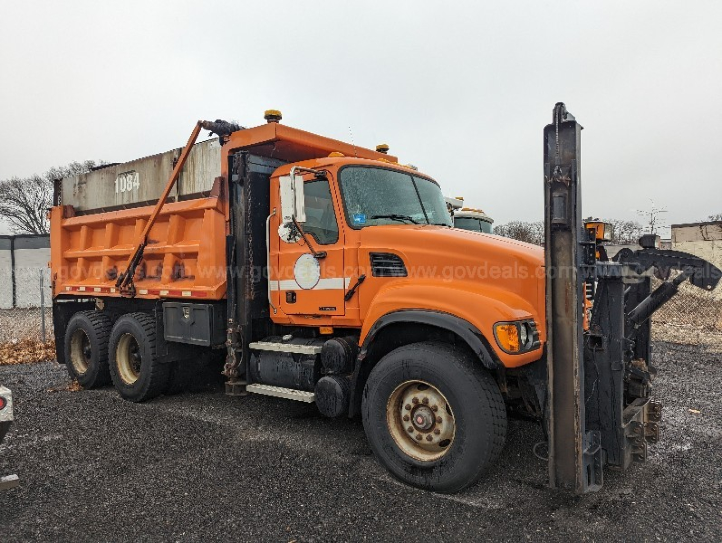 Orange Mack CV713 Granite truck with front-mounted forklift attachment and large dump bed, side view