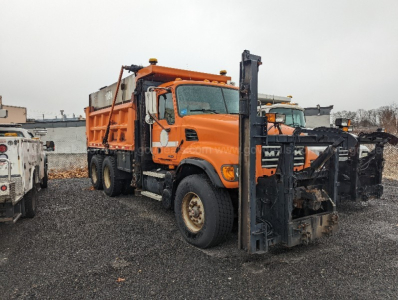 Orange 2004 Mack CV713 Granite plow truck side view showing front plow and salt spreader, VIN visible from photo, stock number in listing.