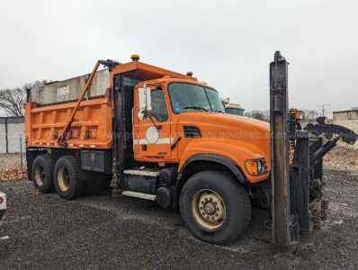 Orange Mack CV713 Granite truck with front-mounted forklift attachment and large dump bed, side view