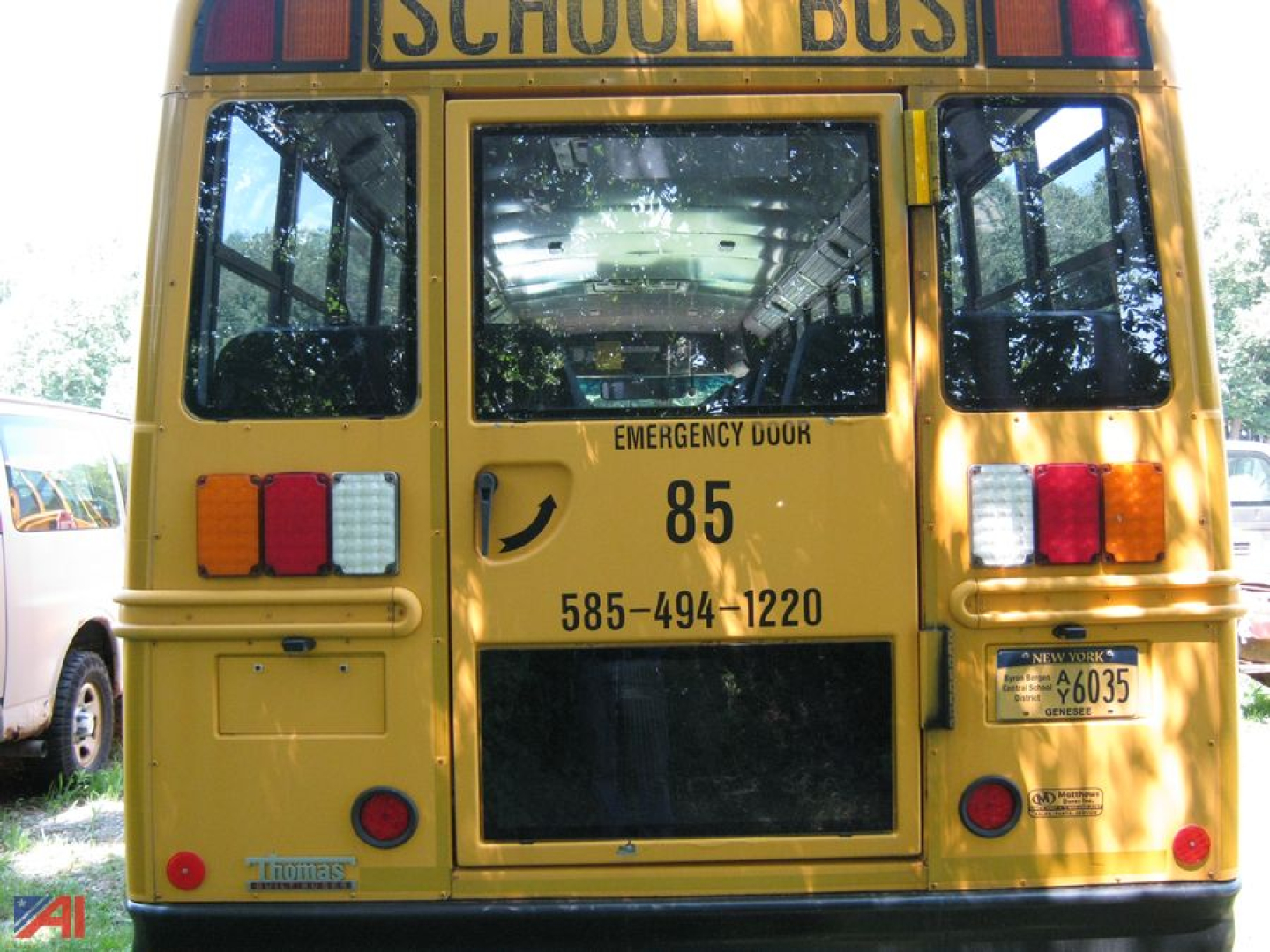 Back of a yellow Freightliner C2 school bus showing emergency door, 85, phone number 585-494-1220, and school bus signage.