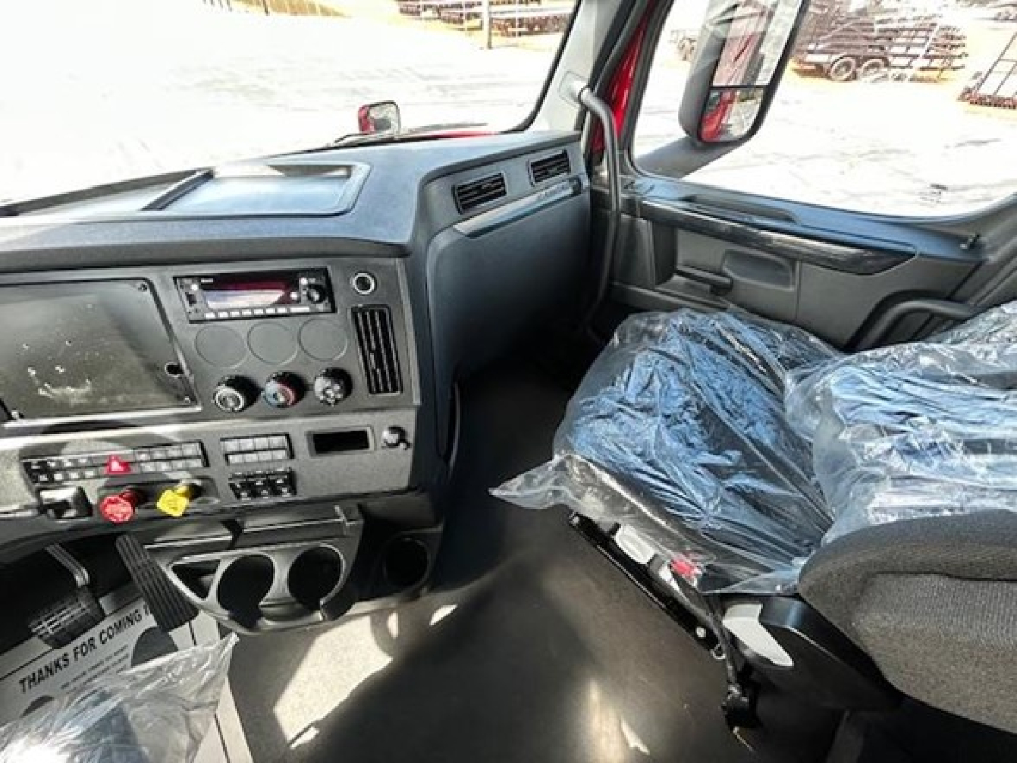 Cab interior of a Freightliner Cascadia 126 truck showing dashboard with radio, climate controls, cup holders, and plastic-covered seat.