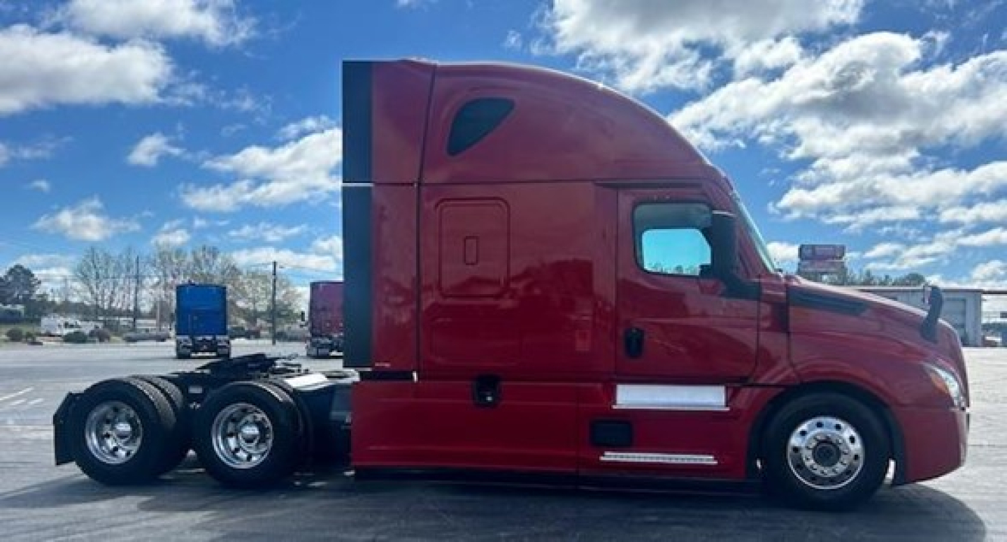 Semi truck side view showing Freightliner Cascadia sleeper cab with red paint and dual rear axles.
