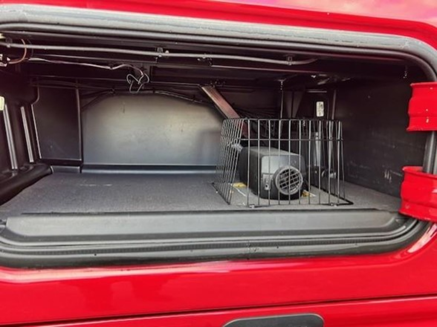 Trunk/compartment view of a 2023 Freightliner Cascadia 126 with a small engine or power unit inside a ventilated crate and a metal barrier.