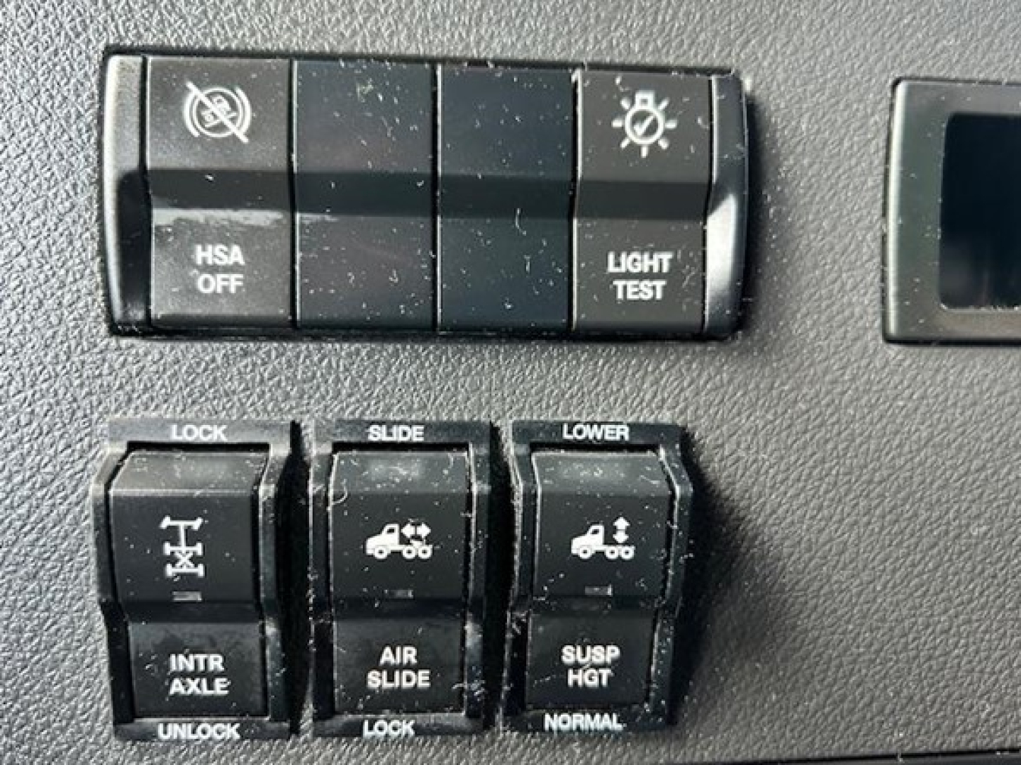 Truck cabin control switches panel with HSA OFF, LIGHT TEST, LOCK, SLIDE, LOWER, INTR AXLE, AIR SLIDE, SUSP HGT indicators