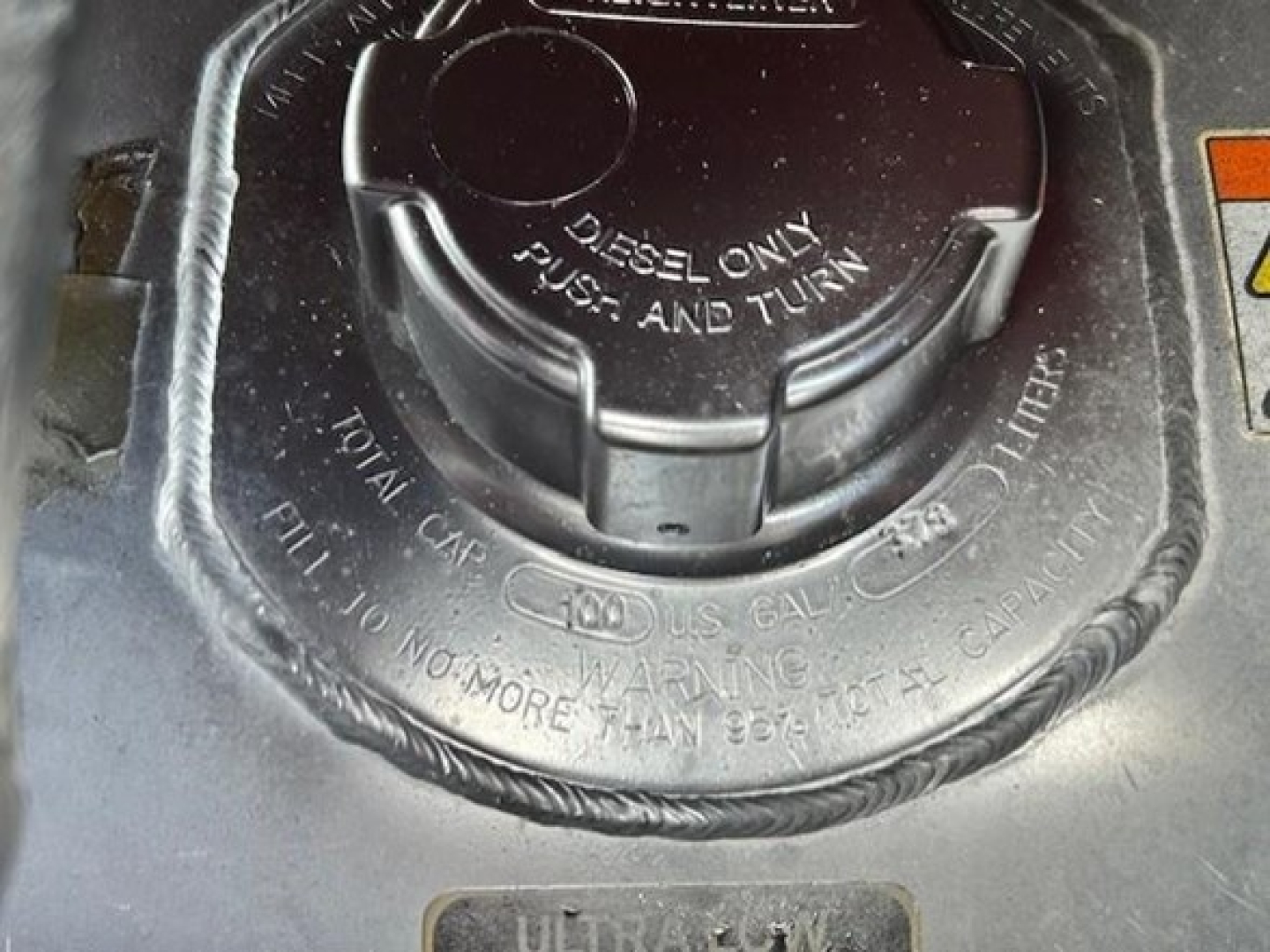 Diesel fuel cap near warning label on Freightliner Cascadia engine bay, cap reads 'DIESEL ONLY' and 'PUSH AND TURN' with surrounding hoses