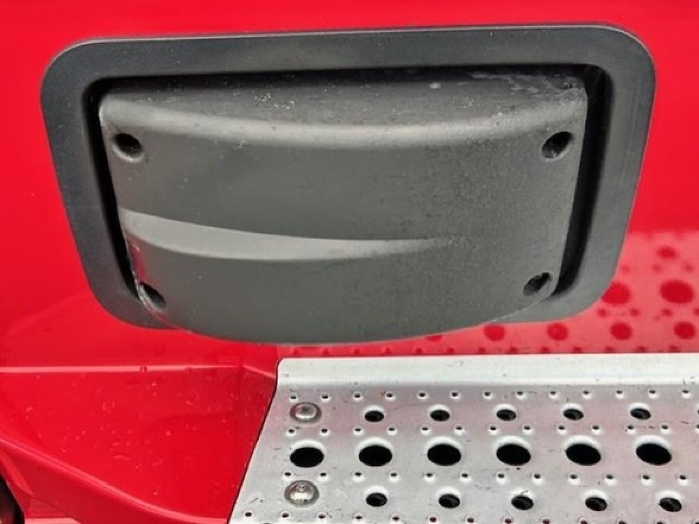 Truck exterior image showing a plastic fuel/maintenance hatch on a red Freightliner Cascadia with textured metal step board beneath.
