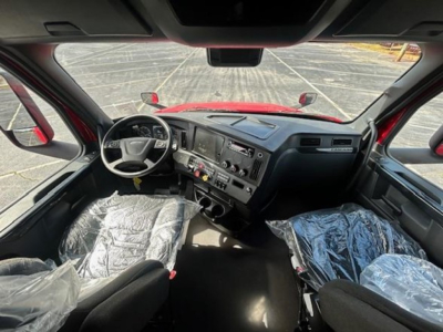 Cab interior of a 2023 Freightliner Cascadia 126 with plastic-covered seats and dashboard controls visible.
