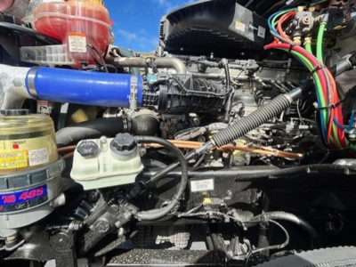 Freightliner Cascadia 126 engine bay showing blue silicone hose, coolant reservoir, various wiring harnesses, and diesel engine components.
