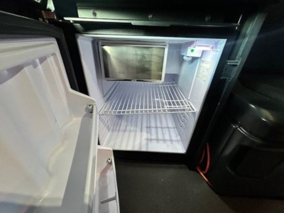 Fridge/freezer in sleeper cab of a Freightliner Cascadia 126 tractor-trailer with open door and empty shelves.