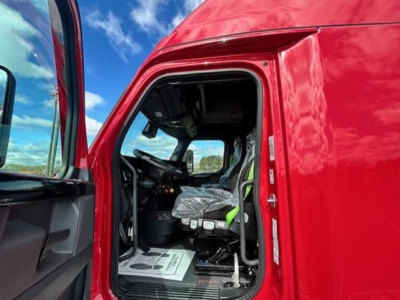Cab interior of a red Freightliner Cascadia truck showing the driver seat and dashboard from open door.