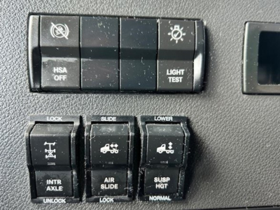 Truck cabin control switches panel with HSA OFF, LIGHT TEST, LOCK, SLIDE, LOWER, INTR AXLE, AIR SLIDE, SUSP HGT indicators