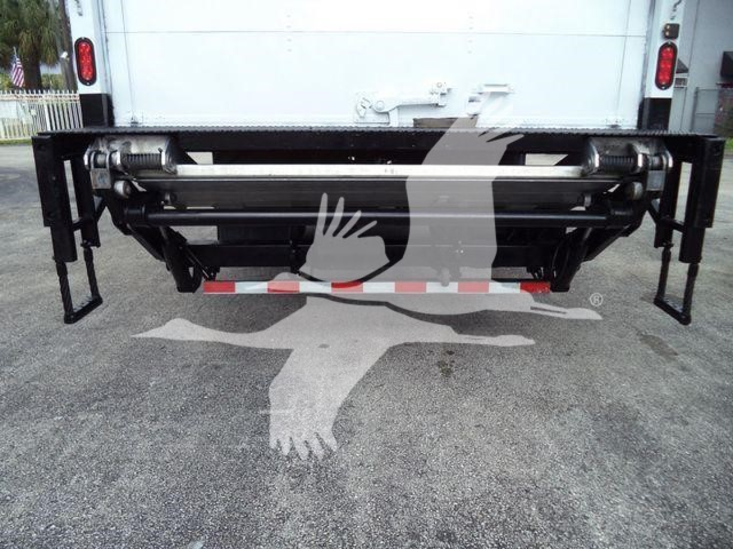 Rear view of a box truck showing a hydraulic lift/ram assembly under the cargo area, with metal support brackets on both sides.