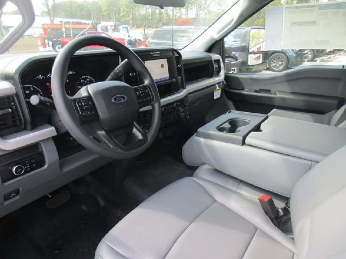 Interior of a Ford F-550 cab showing steering wheel, dashboard with digital display, center touchscreen, and light gray cloth seats. Visible cup holder in center console.
