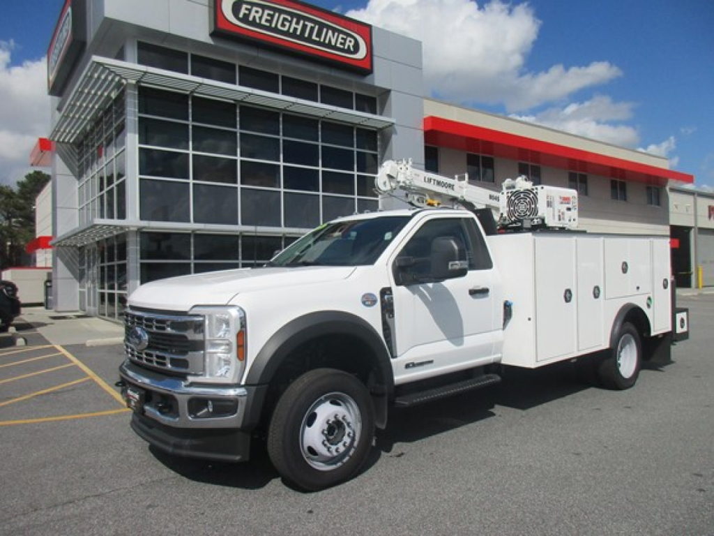 Ford F-550 service utility truck in front of Freightliner dealership showing utility bed with compartments and crane, white cab.
