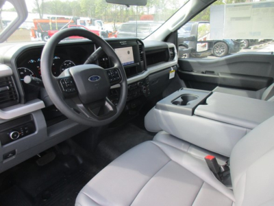 Interior of a Ford F-550 cab showing steering wheel, dashboard with digital display, center touchscreen, and light gray cloth seats. Visible cup holder in center console.