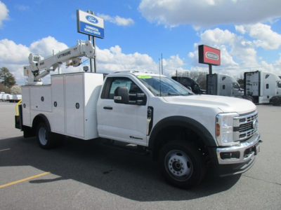 Ford F-550 utility service truck with crane lift, white cab and service body, displayed in a dealership lot.