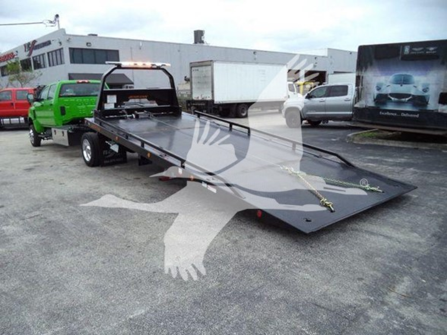 Flatbed tow truck bed on a new 2023 International CV rollout with hydraulic ramps and winch, shown in an outdoor lot.