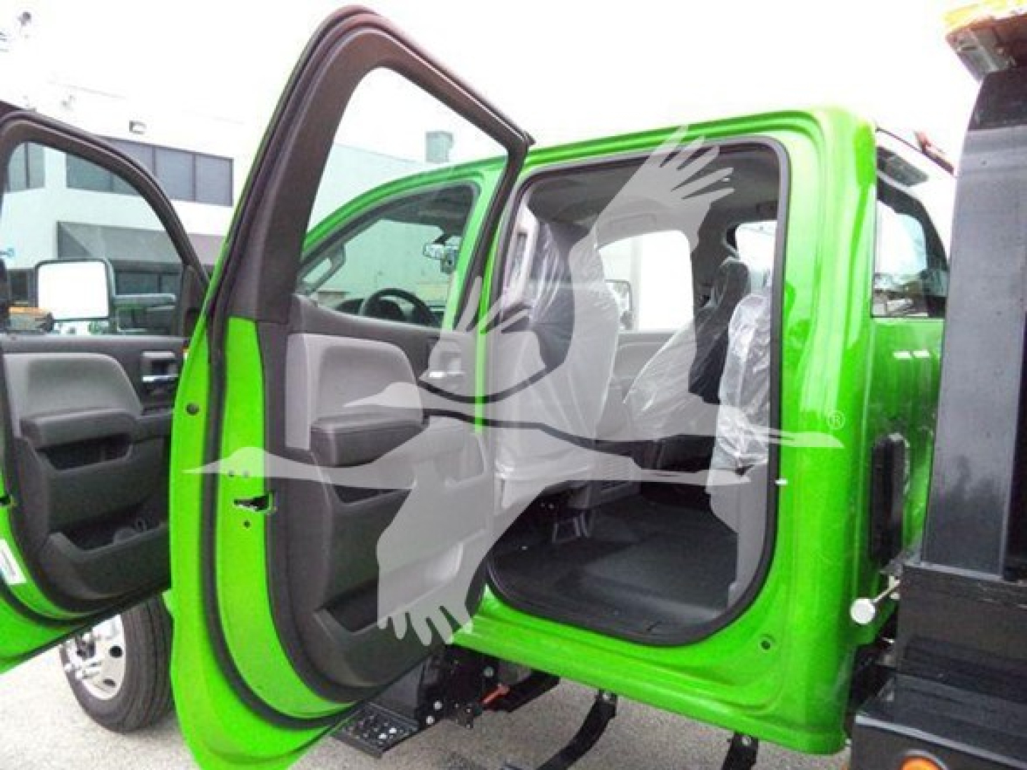 Vehicle interior with front doors open; bright green cab with black interior, side doors open, white overlay watermark of a bird. No visible model text.