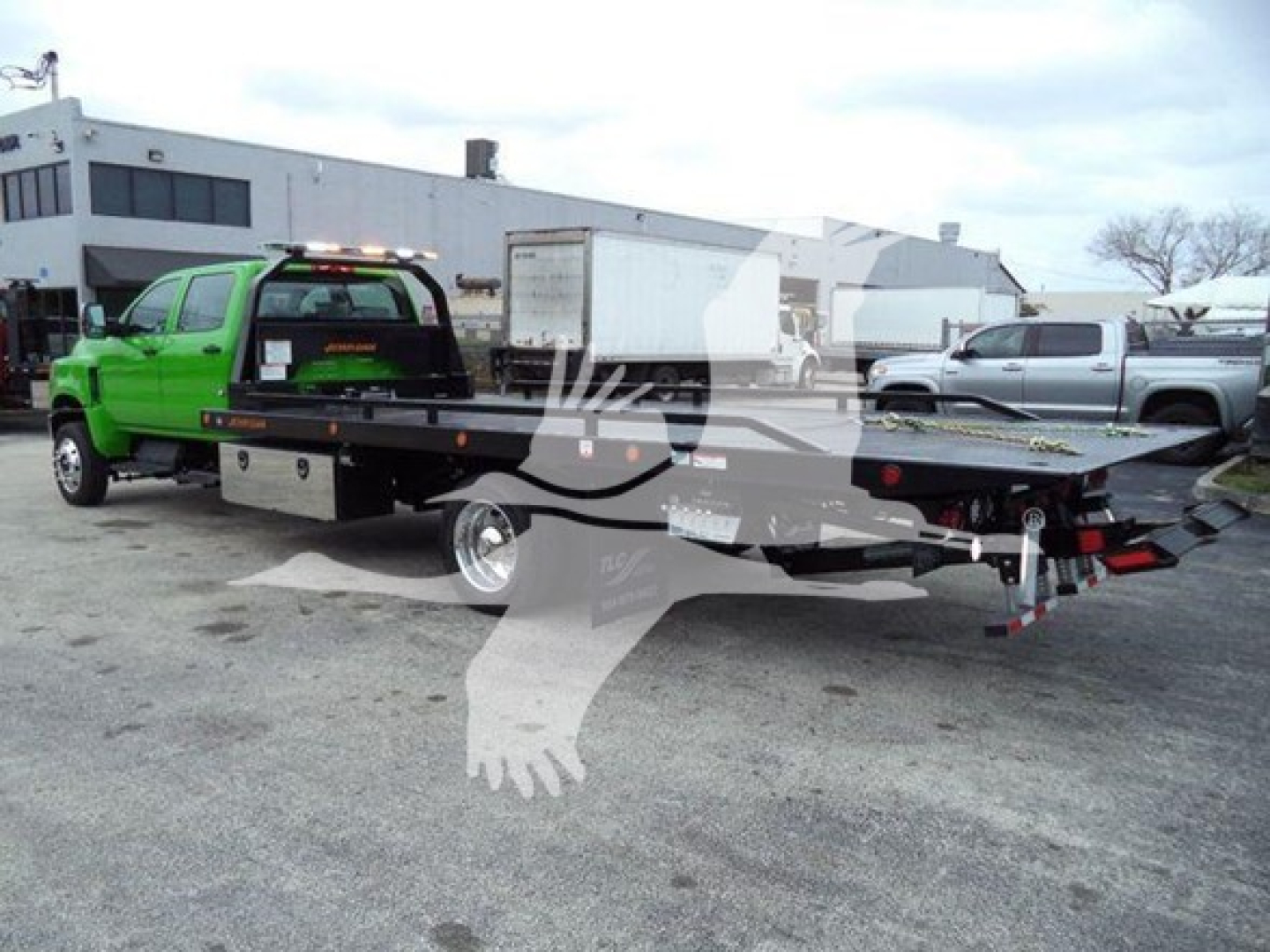 Green International CV rollback tow truck with flatbed and black chassis shown from rear-left side.