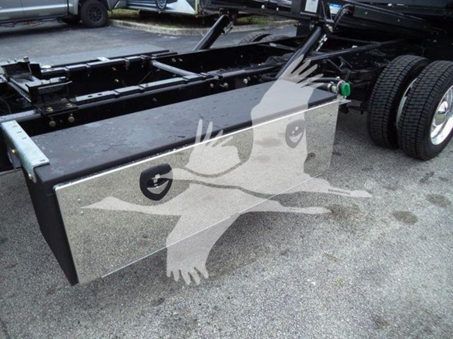 Truck bed toolbox and chassis frame of a 2023 International CV rollback truck showing a rectangular storage box mounted on the frame with a metal latch and mounting points.