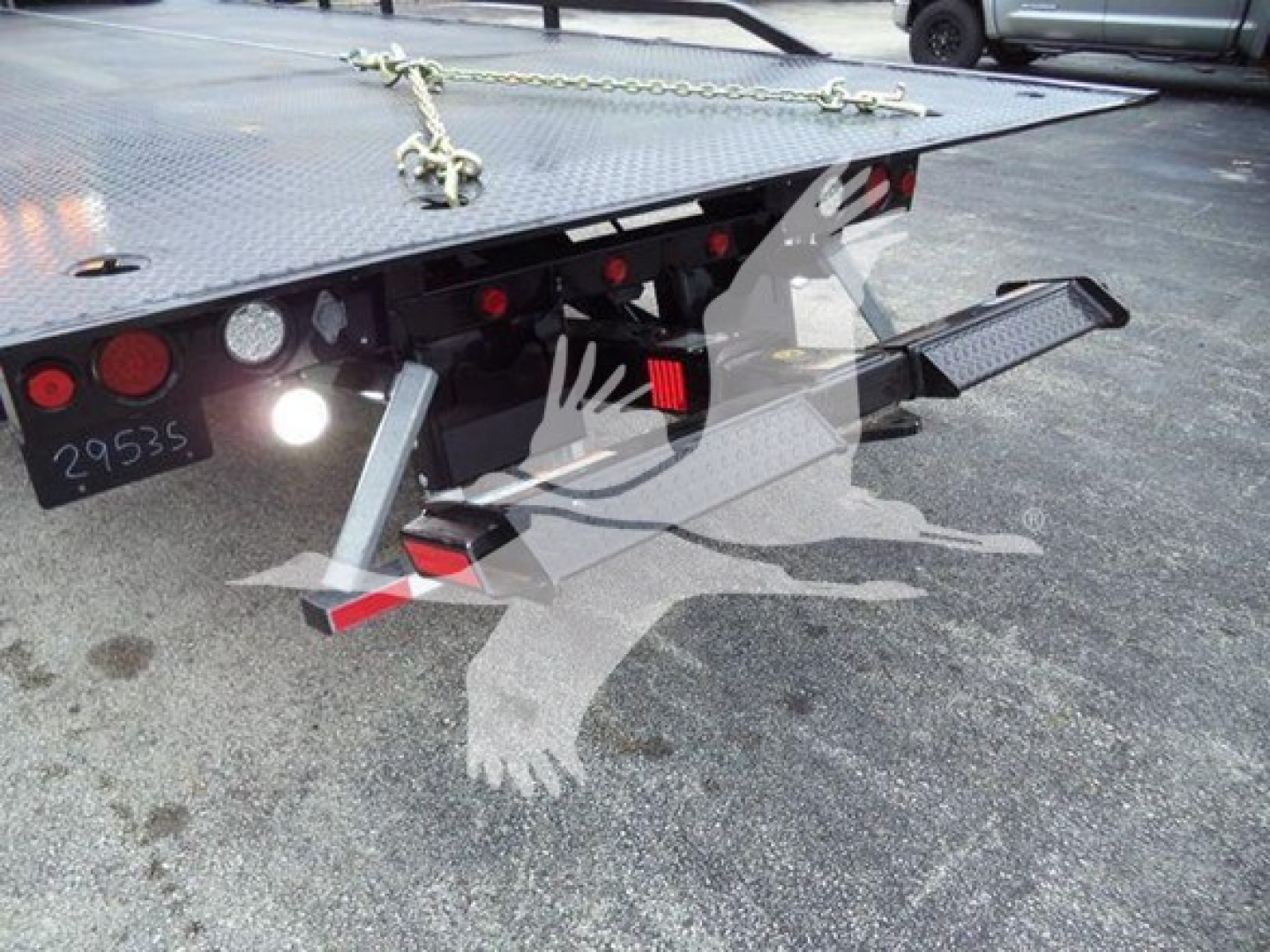 Tractor/utility rollback trailer hitch and rear deck with support legs and safety chains visible.