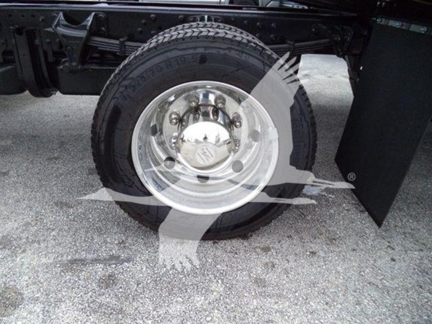 Wheel hub and tire on a truck with chrome wheel and center cap, visible bolts and lug nuts, part of the truck frame and mudflap visible.