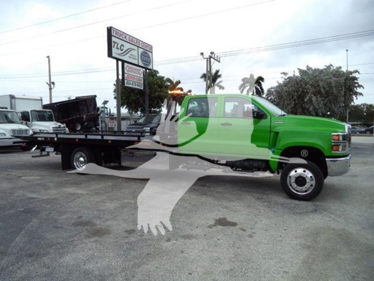 Truck in a dealership lot: green 2023 International CV rollback tow truck with a long flatbed; watermark silhouette across image. Visible text on signboard in background.