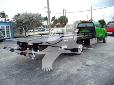 Flatbed tow truck in green cab with black bed, rear view showing warning decals and taillight housings.