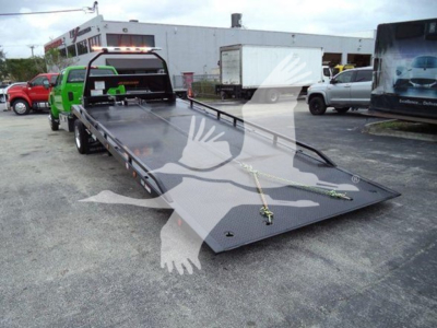 Tow truck rollback flatbed with loading ramps and hoist securing chains, International CV in background.