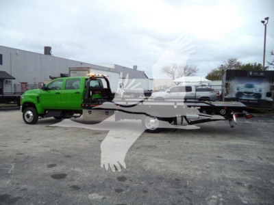 Truck hauler with green tow truck and rollback in lot; text on image not clearly legible