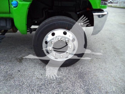 View of front left wheel and fender of a bright green truck, chrome wheel with multiple lug bolts, tire visible, fender and part of bumper.