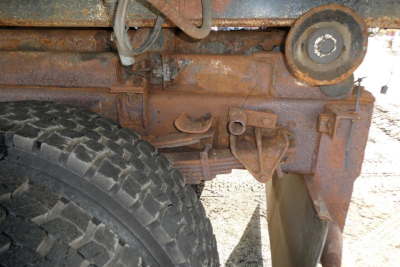 Rusty hooklift truck frame with spare wheel and hydraulic components visible undercarriage of 1999 International 2554 back portion.