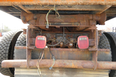 Rear view of a rusted hooklift truck chassis showing two red taillights and wiring harnesses.
