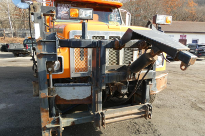 Front of a 1999 International 2554 hooklift truck with mounted hooklift arm and metal frame, orange cab, and warning labels visible.
