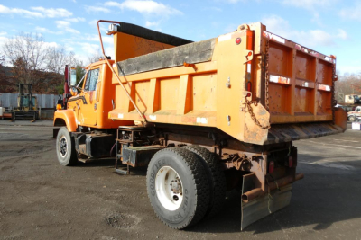 Orange International truck with a large dump bed and hydraulic hooklift, viewed from the side-rear, showing the cargo bed and rear wheels.